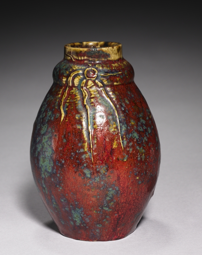 A red pear-shaped vase with scattered blue and dark patches below a narrow rim.