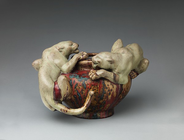 Two pale panthers curl around a rounded bowl with red and blue glaze.